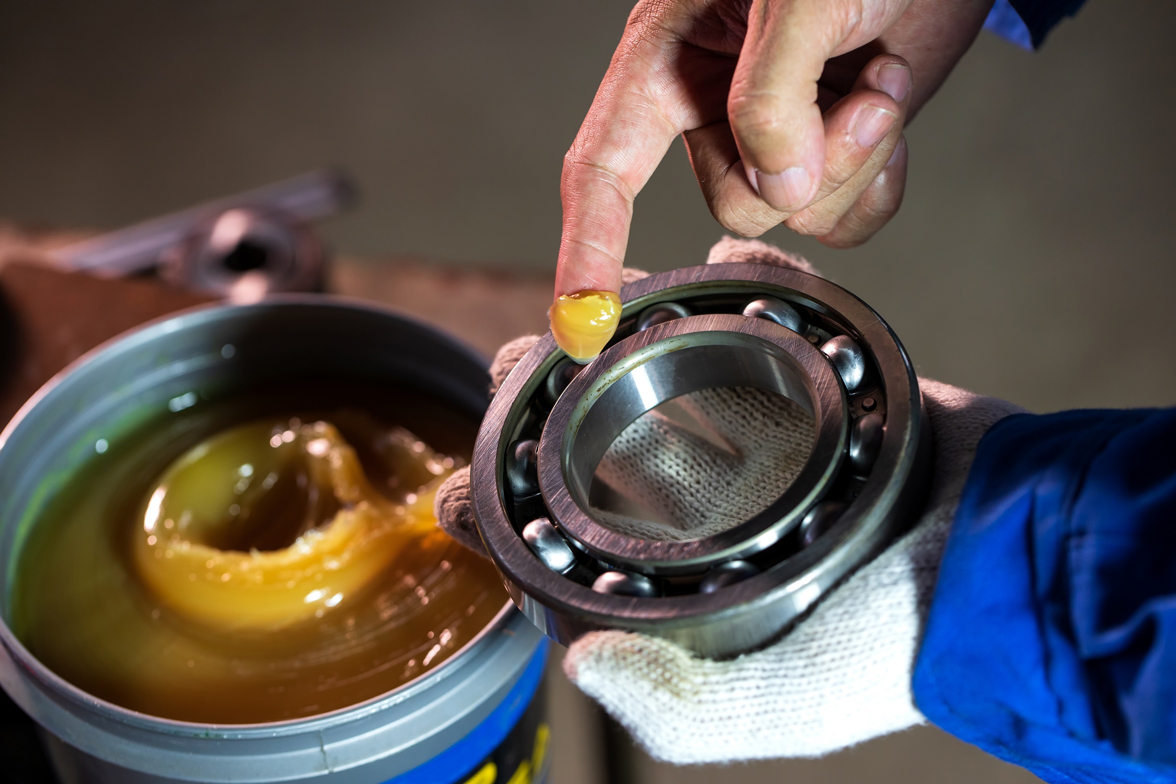 Mechanic is putting lubricant grease into ball bearing in a factory.